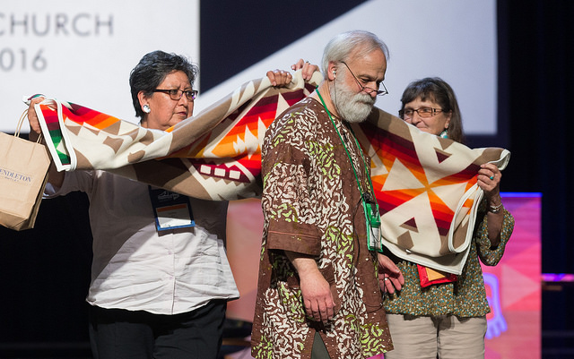 The Rev. L. Fitzgerald “Gere” Reist II (center) is honored for his years of service as secretary of the United Methodist General Conference during the denominational meeting May 20 in Portland, Ore. Presenting him with a blanket are Cynthia Kent (left) and Raggatha Calentine. Photo by Mike DuBose, UMNS