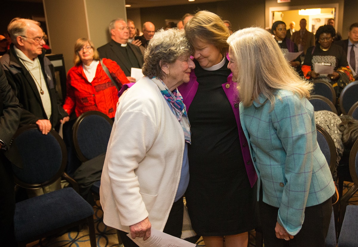 Bishop Karen Oliveto (center, standing) shares a moment with her mother, Nelle Oliveto (left) and her wife, Robin Ridenour, after a hearing before the United Methodist Judicial Council meeting in Newark, N.J. The denomination's top court heard arguments on a petition questioning whether a gay pastor can serve as a bishop in The United Methodist Church. Any decision on that petition could affect Oliveto, the denomination’s first openly gay bishop. Photo by Mike DuBose, UMNS.
