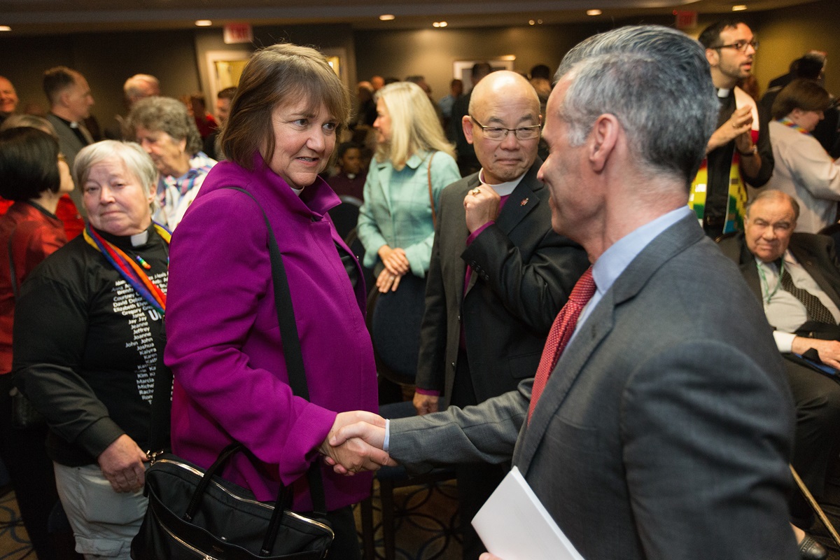 Bishop Karen Oliveto (left) and the Rev. Walter Fenton (right) shake hands during the April 25 oral hearing before the United Methodist Judicial Council meeting in Newark, N.J. Fenton is the analyst for Good News, which advocates that the church hold the line on homosexuality teachings. Photo by Mike DuBose, UMNS