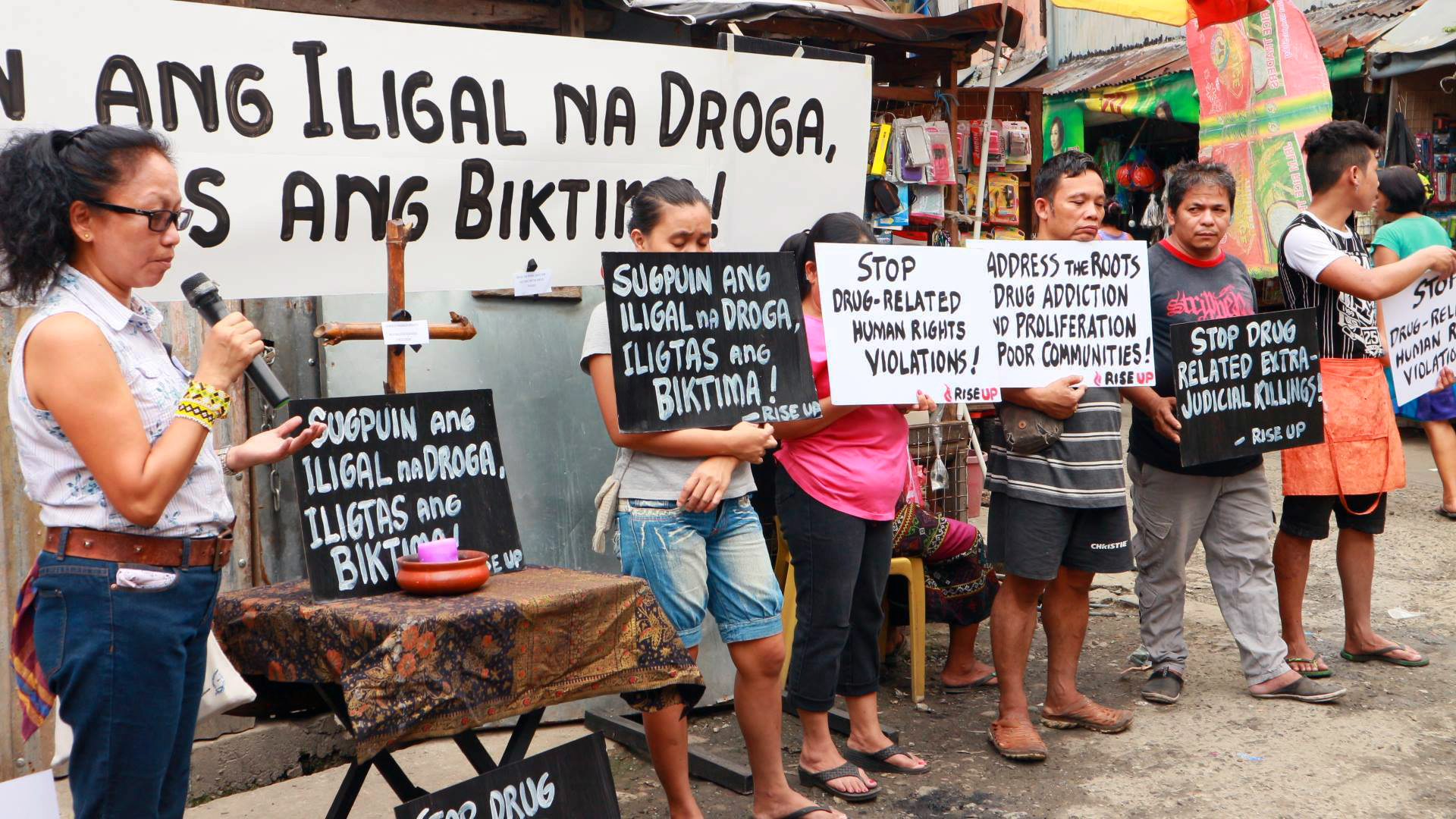 In a file photo from December 2016, Norma Dollaga, on left with microphone, speaks during an ecumenical action of Kadamay: Stop the Killings, a community organization that advocates for the poor in urban communities, in Quezon City, Philippines. The placards in Filipino say, "Dismantle illegal drugs, Save the victims!" Photo courtesy of Norma Dollaga.