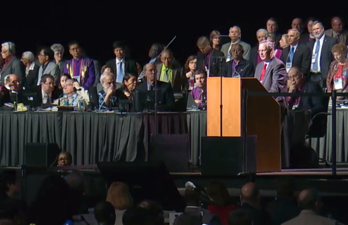 In a video file image, Bishop Bruce R. Ough, at podium, delivers a statement from the Council of Bishops about the formation of the Commission on a Way Forward during the 2016 General Conference in Portland, Ore. Video image courtesy of United Methodist Communications.