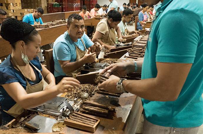 A worker stops by each station to collect the hand-rolled cigars and take them to the next area to be packed in cellophane sleeves, labeled and boxed. Photo by Kathy L. Gilbert, UMNS.