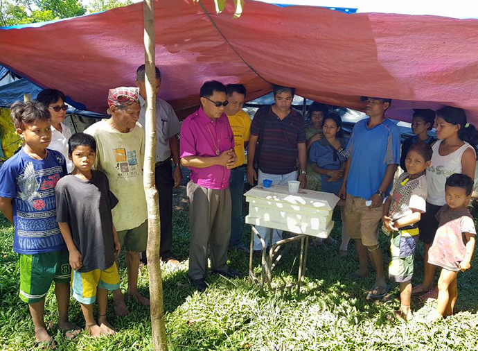 Bishop Rodolfo A. Juan (center in pink shirt) prays with the bereaved family of a baby who was born — and died — at a refugee camp in Malaybalay, Philippines. The camp in northern Mindanao was set up after an outbreak of violence against Lumads (indigenous peoples). Photo courtesy of Dan Ela.
