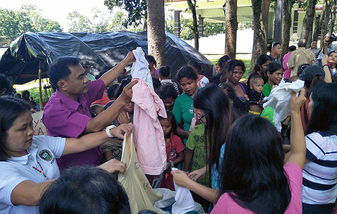 Articles of clothing are among relief items distributed by United Methodists, including Bishop Rodolfo A. Juan (second from left), to Lumads fleeing violent conflicts in the Philippines. The bulk of the items were donated by Korean churches. In the background stands the tent where the Lumads are camping out near the capitol grounds in Malaybalay. Photo courtesy of Dan Ela.