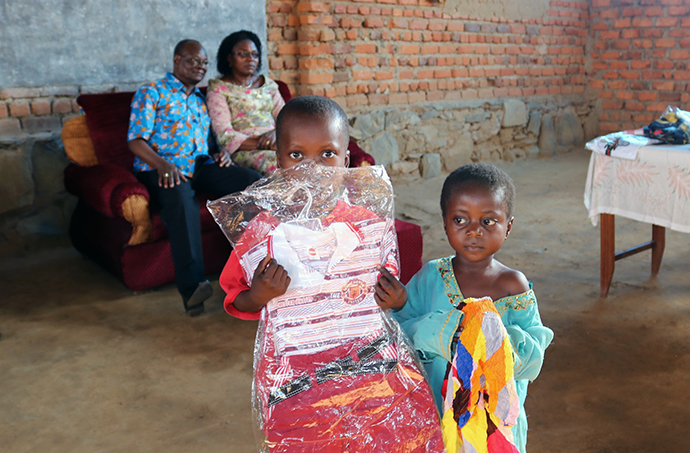 Two orphans who were brought from the Kasongo-Samba District of the Democratic Republic of Congo to Kindu hold up clothing they received. In addition to providing supplies for those displaced by rebel violence, the church team also helped relocate some widows and orphans. East Congo Area Bishop Gabriel Yemba Unda, along with his wife, Marie Claire Unda, are seated in the background. Photo by Judith Osongo Yanga, UMNS.