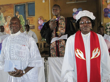 Bishop John Yambasu (in background) presents the Rev. Mariama Bockari (right), supported by husband, the Rev. David Bockari (left), to the Makeni congregation upon her induction as district superintendent.