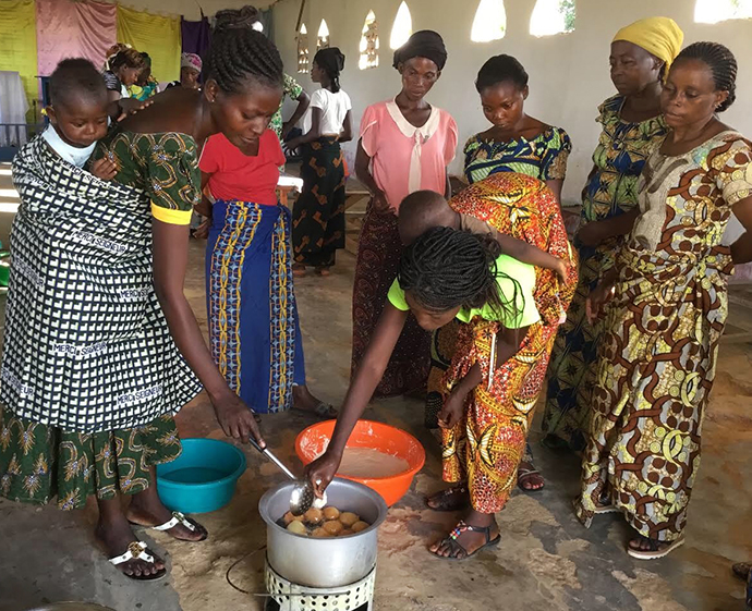 A group of women, some with babies and children, check cakes in a pot while learning cooking techniques during training provided at Kindu United Methodist University in the Democratic Republic of Congo. While their husbands are studying theology, the wives are given training to support their husbands in their pastoral ministry through improved domestic and literary skills. Photo by Judith Osongo Yanga, UMNS.