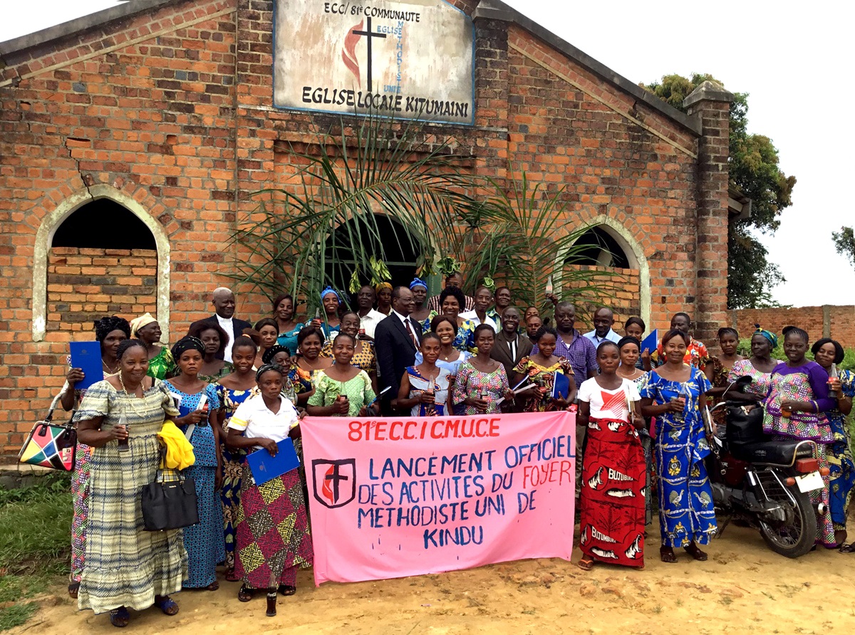 A group poses for a photo with Bishop Gabriel Yemba Unda (center, left behind banner) outside Kitumaini United Methodist Church during training provided for the wives of future pastors who are attending Kindu United Methodist University in the Democratic Republic of Congo. The East Congo Episcopal Area organizes the faculty of theology and provides classes in several trades, languages, culinary sciences, hygiene and more for the women while their husbands are in school at the university. Photo by Judith Osongo Yanga, UMNS.
