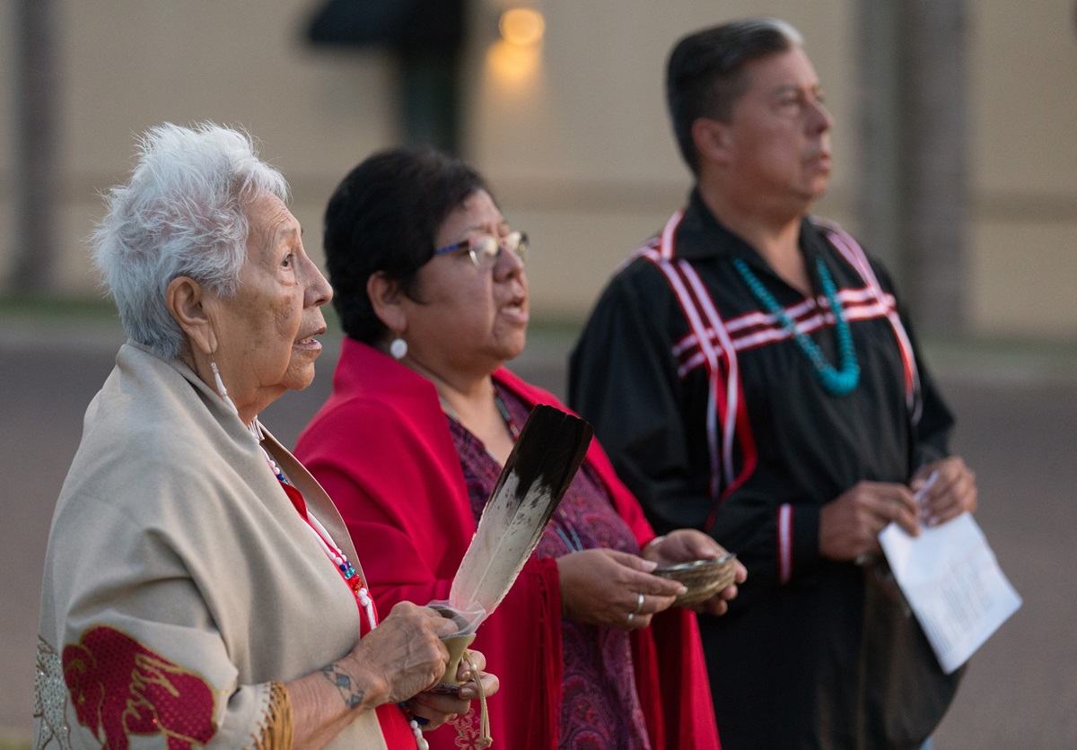 Native American scholar Henrietta Mann (left) and leaders of The United Methodist Church’s Oklahoma Indian Missionary Conference, the Revs. Donna Pewo (center) and David Wilson, conduct a prayer ceremony for immigrant children held at the Casa Padre detention facility in Brownsville, Texas. The three prayed in a grassy median outside the facility, a former Walmart. It is the largest shelter in the U.S. for minors caught crossing the border illegally. Photo by Mike DuBose, UMNS.