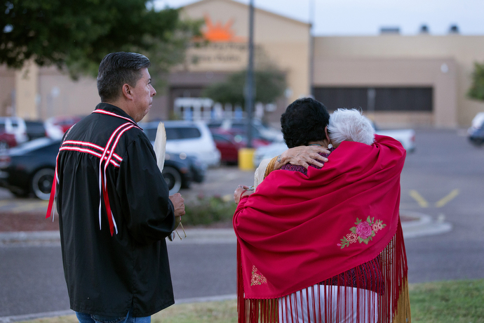 The Rev. Donna Pewo (wearing red shawl) embraces Henrietta Mann following a prayer service for immigrant children held at the Casa Padre detention center, visible behind them. At left is the Rev. David Wilson, superintendent of The United Methodist Church’s Oklahoma Indian Missionary Conference. Photo by Mike DuBose, UMNS.