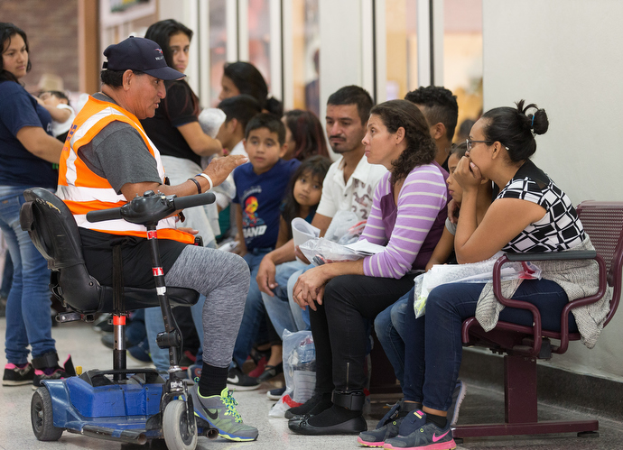 Volunteer Luis Guerrero (on scooter) gives immigrants a lesson in how to navigate the U.S. bus system at the station in McAllen, Texas. Guerrero is an ex-firefighter who lost one of his legs in the line of duty. He comes to the bus station almost every day to help. Photo by Mike DuBose, UMNS.
