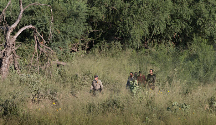 A U.S. Border Patrol agent escorts a group of people who were caught entering the U.S. illegally from their hiding place in a heavily wooded area near McAllen. Photo by Mike DuBose, UMNS.