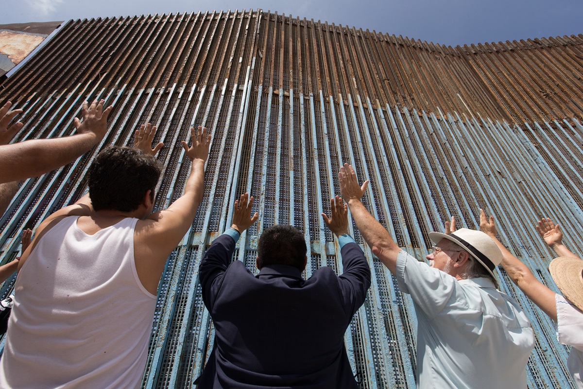 The Revs. Joel Hortiales (center, in blue blazer) and David Farley (to Hortiales' right) join parishioners of the Border Church in Tijuana, Mexico, as they lift their arms skyward beneath the fence that marks the border with the U.S.