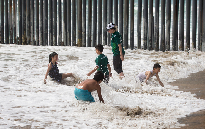 A family plays in the surf alongside the Mexico - U.S. border fence at El Faro Park on the Mexican side of the border. Photo by Mike DuBose, UMNS.