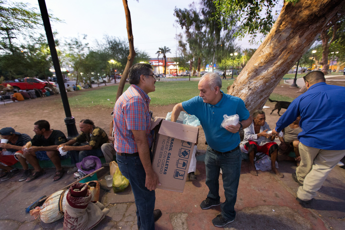 Bishop Felipe Ruiz Aguilar of the Methodist Church of Mexico (holding box) and Victor Rodriguez of El Divino Redentor Methodist Church help serve dinner to migrants and others living on the street at Mariachi Plaza. Photo by Mike DuBose, UMNS.
