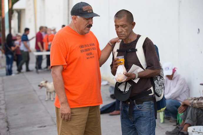 Javier Trejo (left) from La Santísima Trinidad Methodist Church offers breakfast and a prayer to Candalario Tapia who is living on the street in Mexicali.