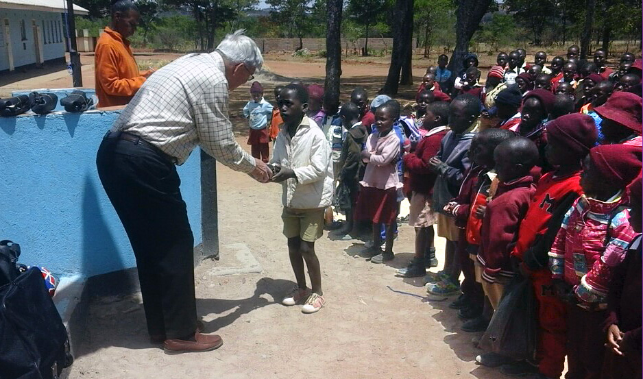 Charlie Moore hands a pair of shoes to a student at Hanwa Mission School in the Murewa District  of Zimbabwe. Moore brought 50 pairs of shoes and a dozen soccer balls to hand out to the students as part of a partnership between Community United Methodist Church in Crofton, Maryland, and the Zimbabwe West Conference. A fifth-grade class from Crofton Elementary in Maryland donated the items. Photo by Chenayi Kumuterera, UMNS.