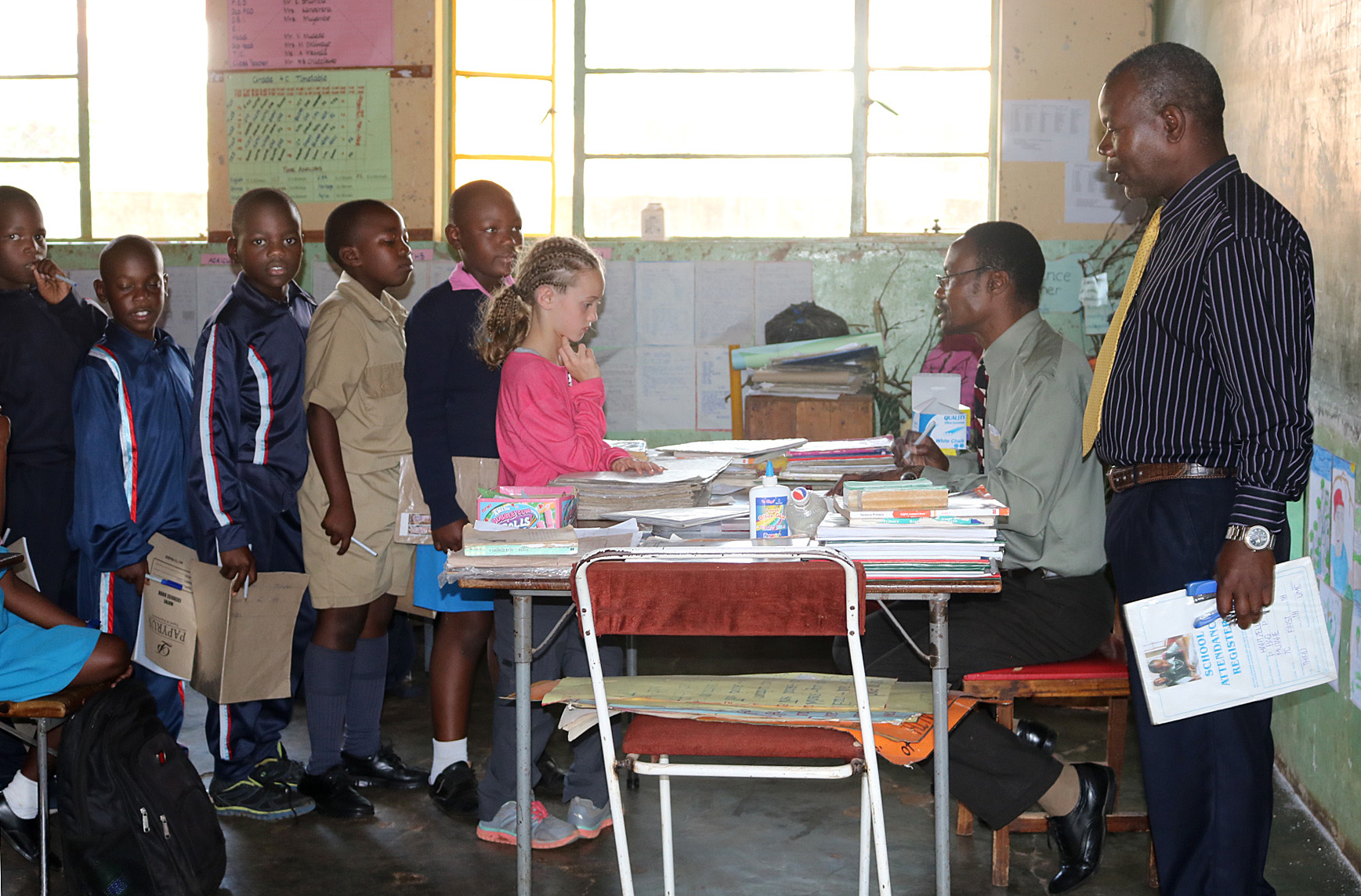Mikayla Jaissle (center, wearing pink shirt) stands in line with other students while teacher Nicholas Chidzikwe checks her work at Hartzell Primary School in Mutare, Zimbabwe. The 10-year-old from Lakewood, Ohio, accompanied her mother, the Rev. Laura Jaissle, on the trip and attended class at the United Methodist school for two days. Photo by Eveline Chikwanah.