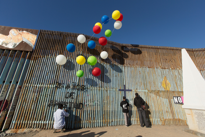 During a Posada celebration at El Faro Park in Mexico, people peer through the border fence that separates the U.S. from Mexico while a volunteer affixes a sign celebrating the 25th anniversary of La Posada Without Borders.