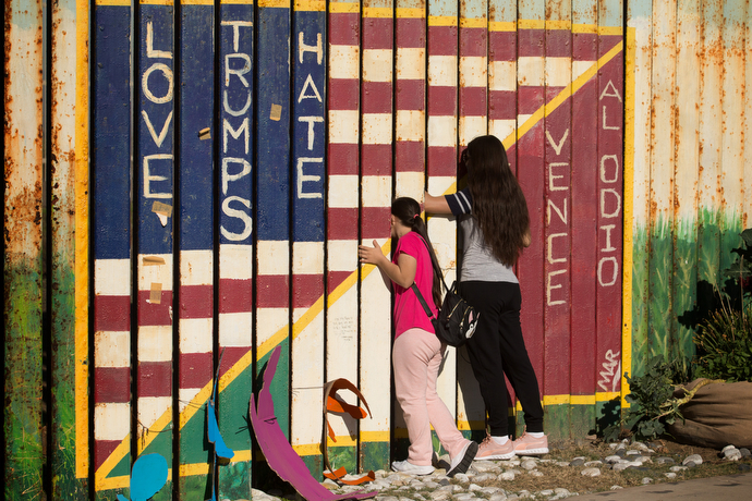 During a Posada celebration at El Faro Park in Tijuana, Mexico, people peer through a section of the U.S.-Mexico border fence that is decorated with a message of love in two languages.