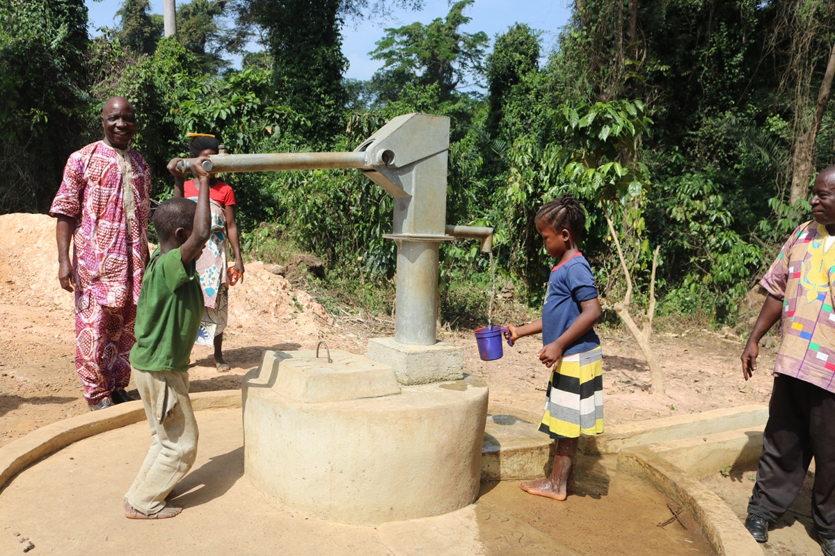 Dolo Boamou and Denise Kpoghomou pump water from a well as adults look on in Yassata, Guinea. The United Methodist Church in Liberia is building five wells in the country as part of its Water for Life project. Photo by E Julu Swen, UMNS.