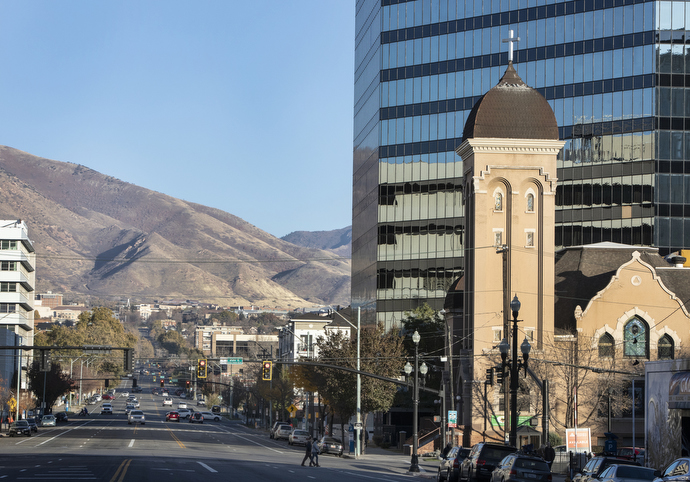The historic church tower of First United Methodist Church in Salt Lake City contrasts with nearby modern buildings and Wasatch Mountains. 