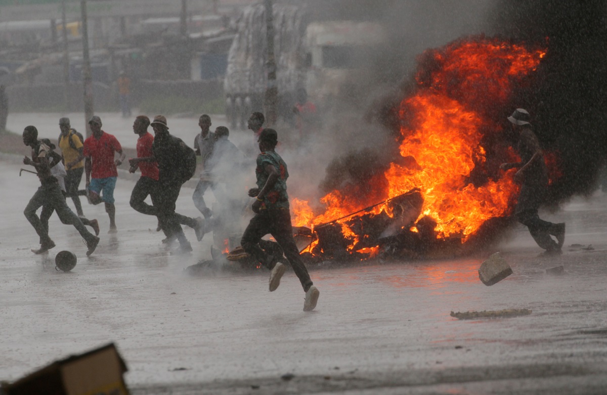 La gente corre en una protesta mientras las barricadas se queman en medio de una intensa lluvia en la ciudad capital de Harare, Zimbabue. Los/as metodistas unidos/as están pidiendo oraciones por la paz en medio de los enfrentamientos entre los/as manifestantes y las fuerzas de seguridad tras un aumento en los precios del combustible. Foto por Philimon Bulawayo, Reuters. No reutilizar. Uso único.