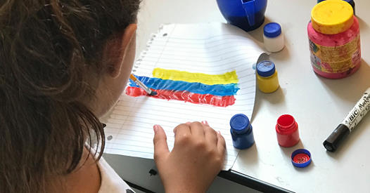Hailey pinta una bandera venezolana durante el tiempo de clases de  artes y manualidades, con niños/as del refugio en Boa Vista. Foto: Emily Everett, GBGM.