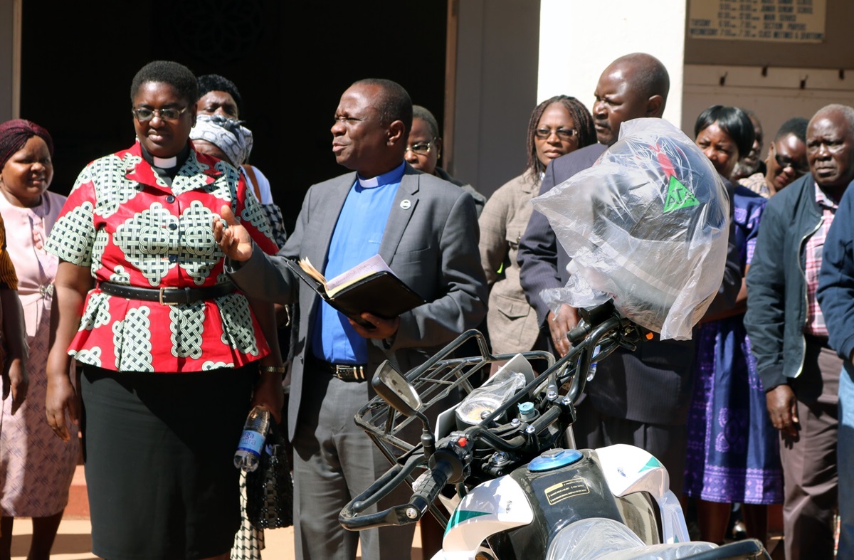 The Rev. Alan Masimba Gurupira (center), officiates a ceremony to present motorbikes to five pastors of the Mutasa Nyanga District of Zimbabwe on July 20. Listening are the Rev. Tafadzwa Musona (left, in red), district superintendent; and the Rev. Duncan Charwadza (right, behind bike), Connectional Ministries director and Deputy Administrative Assistant to the Bishop. The motorbikes were a gift from Mutasa Nyanga Homelink, a group of church members originally from the district, who pool their resources to support the pastors. Photo by  Eveline Chikwanah, UM News.