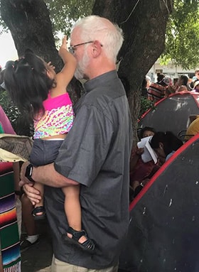 The Rev. Larry Duggins, a United Methodist elder and executive director of the Missional Wisdom Foundation, holds a child from Honduras during a visit to Matamoros, Mexico. Duggins was part of an ecumenical group that went to the border out of concern about a U.S. policy requiring some asylum seekers to remain in Mexico as their cases are considered. Photo Courtesy of Texas Impact.