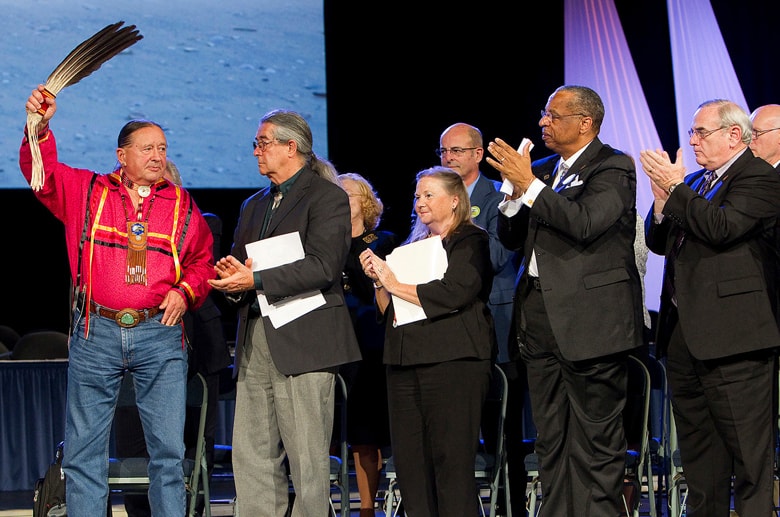 The Rev. George Tinker (left) receives the applause of United Methodist Church leaders after giving the sermon during an "Act of Repentance Toward Healing Relationships with Indigenous Peoples" at the 2012 United Methodist General Conference. Applauding Tinker (from left, front row) are the Rev. Thom White Wolf Fassett and bishops Mary Ann Swenson, Robert E. Hayes Jr. and Larry M. Goodpaster. Mike DuBose, UM News.