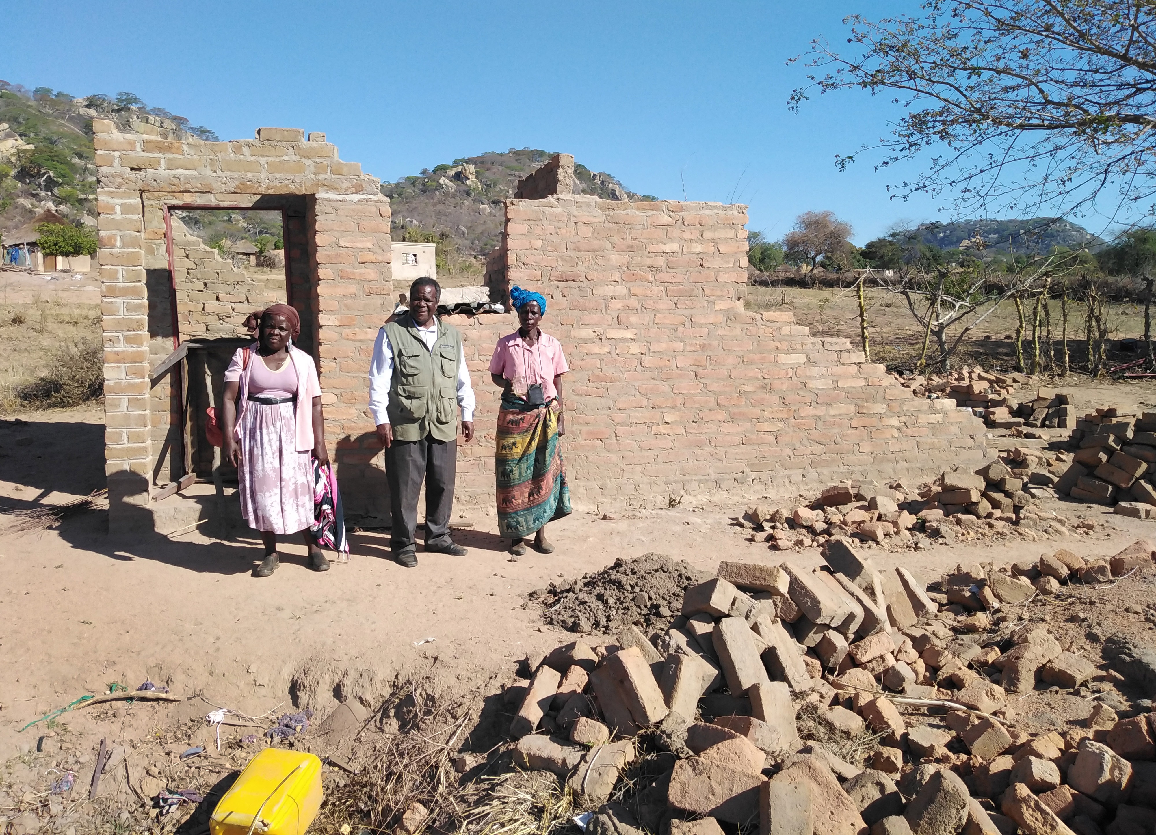Vivian Chigweshe, right, stands in front of her home, which was destroyed by Cyclone Idai in March. She is among the survivors who will have a new house built with support from The United Methodist Church. Standing from left are lay leader Chirobwe Kupeti and the Rev. Jairos Mafondokoto, Masvingo District superintendent.  Photo by Chenayi Kumuterera, UM News. 