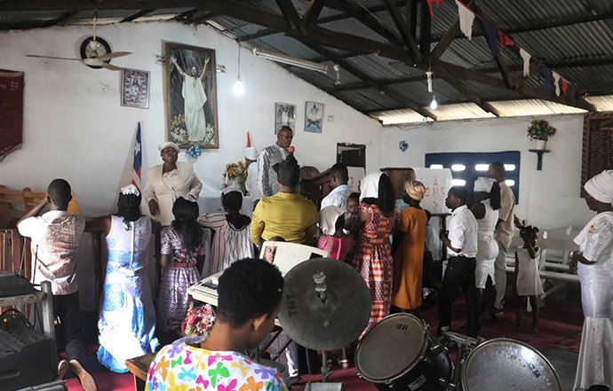 Le Révérend James Y. Kaifunbah (au centre avec le micro) prie pour les membres de l'église Méthodiste Unie de Buduburam (Ghana) pendant le culte du dimanche 3 novembre. L'église, fondée par les Méthodistes Unis qui ont fui le Libéria pendant la guerre civile des années 1990, risque d’être fermée, selon Kaifunbah. Photo de E Julu Swen, UM News.