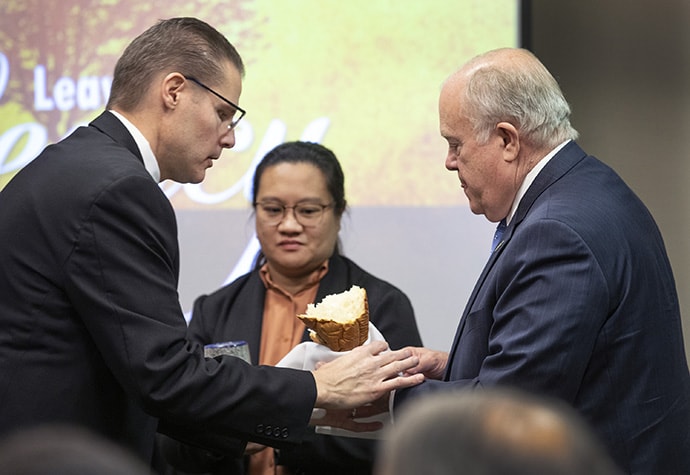 The Rev. Dustin Petz (left) of the Great Plains Conference hands bread to Bishop Michael McKee during the Nov. 15 communion service at the GCFA board meeting. Holding the chalice is board member Regan Reyes de Guzman of the Philippines. Photo by Kathleen Barry, UM News.