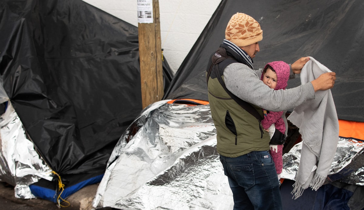 Jesús, a migrant from Michoacán state in Western Mexico, tries to shield his 1-year-old daughter, Kataleya, from a cold drizzle falling at the tent encampment where they are living at the foot of the Paso del Norte Bridge in Juárez, Mexico. Michoacán is among five states in Mexico given the highest-risk “do not travel” warning by the U.S. State Department.