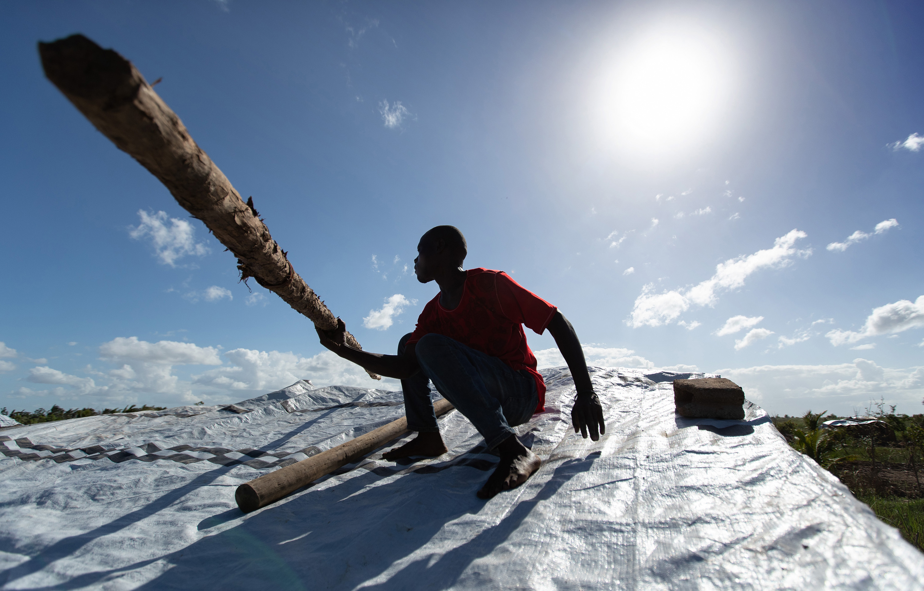 Jorge João Novo soulève un poteau en bois pour aider à fixer une bâche d'urgence sur sa maison après que le toit ait été arraché par le cyclone Idai à Buzi, au Mozambique. Photo de Mike DuBose, UM News.