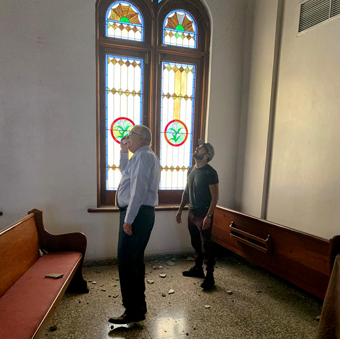 Bishop Hector F. Ortiz (left) of the Methodist Church of Puerto Rico surveys earthquake damage at the Church of the Resurrection in Ponce. The stained-glass windows behind him, previously damaged by Hurricane Maria, were repaired with hurricane recovery funds. Photo courtesy of the Methodist Church of Puerto Rico.