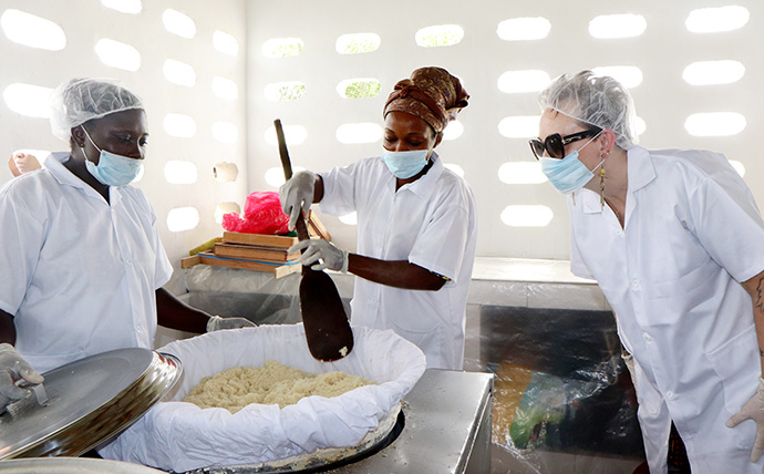 Lorrie King (à droite), directrice du développement durable à UMCOR, regarde Akossi Lobochi Rosine (à gauche) et Ayibé Carine fabriquer de l'attiéké dans une nouvelle usine de transformation à Anyama, en Côte d'Ivoire. L'attiéké est un plat ivoirien fabriqué à partir de farine de manioc dont la texture est similaire à celle du couscous. Photo de Isaac Broune, UM News.