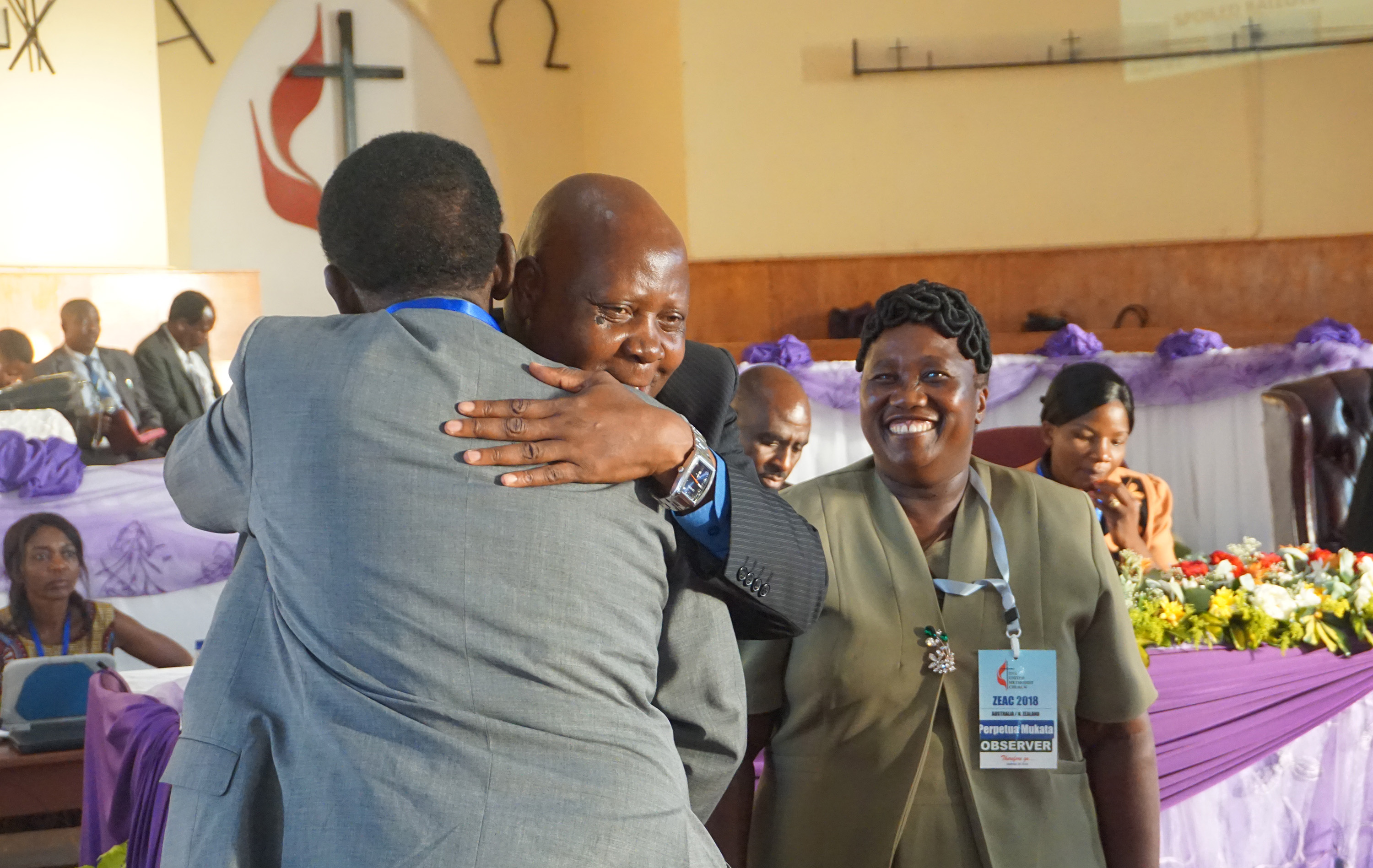 The Rev. Josephat Banda congratulates his new district superintendent of diaspora, The Rev. Stephen Mukata (center), as Mukata’s wife, Perpetua Mukata, looks on at Old Mutare Mission in Mutare, Zimbabwe, during his appointment in 2018. Mukata oversees diaspora in the United Kingdom, Australia, New Zealand and Canada. Photo by Kudzai Chingwe, UM News.