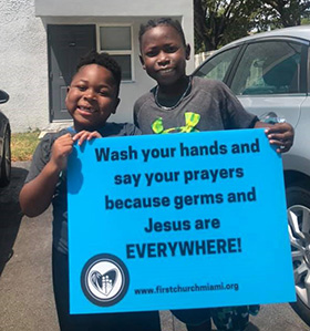 Two young members of First United Methodist Church of Miami hold a sign delivered by the church, intended to win a smile from people struggling to keep their morale up during the COVID-19 pandemic. Photo by The Rev. Audrey Warren, First United Methodist Church of Miami. 
