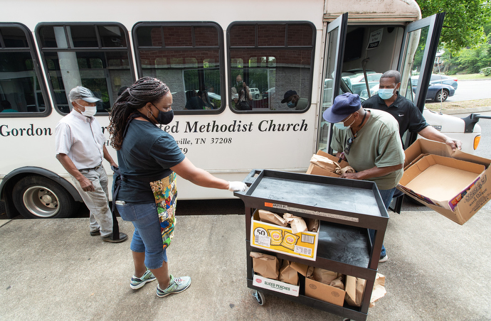 The Rev. Paula Smith (second from left) steadies a cart while volunteers Tim Morgan (in green t-shirt) and Richard Wilson load box lunches for distribution through the Hands of Hope food security program at Gordon Memorial United Methodist Church in Nashville, Tenn. At left is volunteer Matthew Job, 80, who drives the church van for the program. Photo by Mike DuBose, UM News.