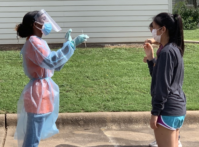 A woman in protective gear holds out a swab to a woman who has come for COVID-19 testing at Cochran Chapel United Methodist Church in Dallas, Texas. Cars lined up early for the June 29 opportunity. Photo by Matt Jacob, North Texas Conference.