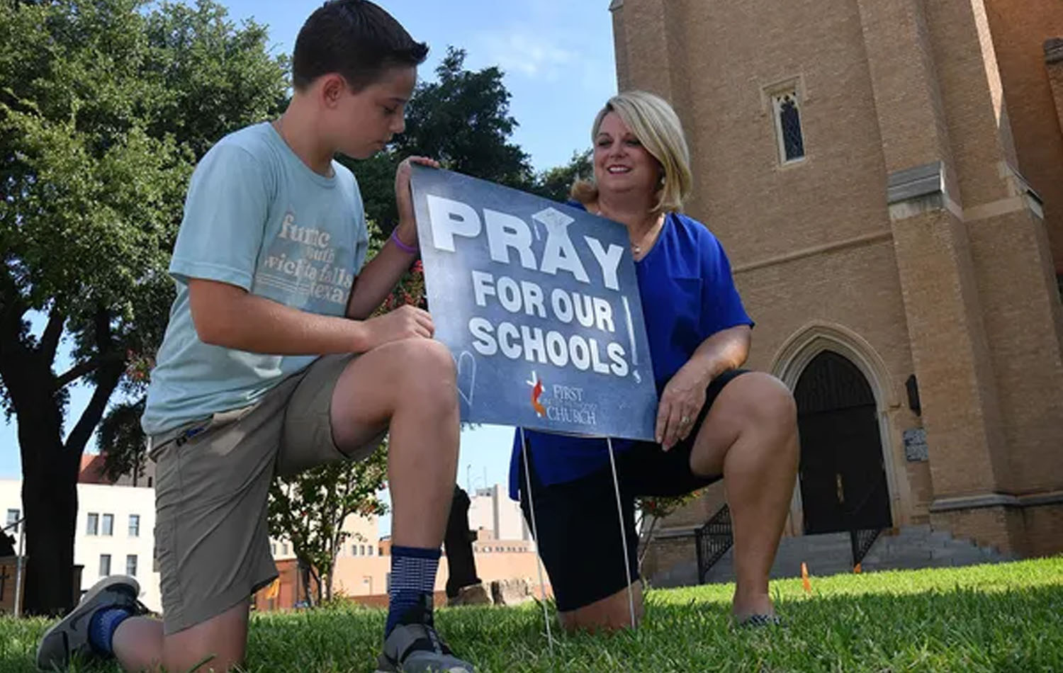 Parker Deal y su madre Joy Deal posan al lado de uno de los carteles “Ore por nuestras escuelas”, distribuido por la Primera Iglesia Metodista Unida. Foto cortesía de Torin Halsey de Times Record News.