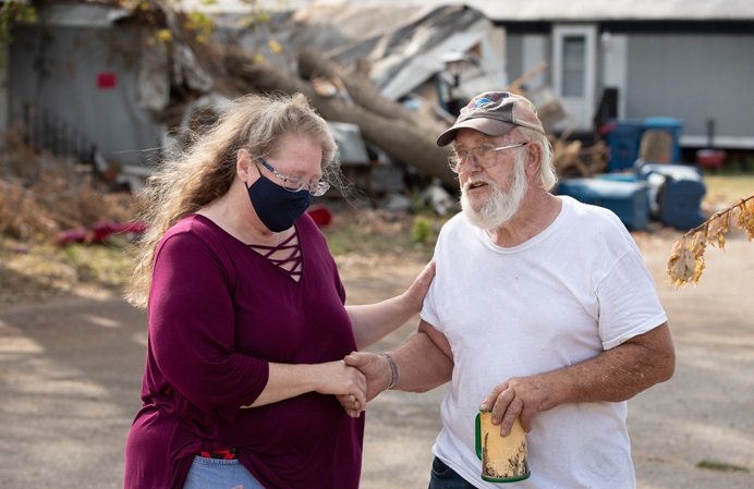 The Rev. Catie Newman prays with John W. Weaver in front of a neighbor’s wind-damaged home while a United Methodist volunteer team makes emergency repairs to his roof in Marion, Iowa. Weaver’s mobile home was severely damaged during a derecho windstorm Aug. 10. Newman is the disaster response coordinator for the Iowa Conference. 