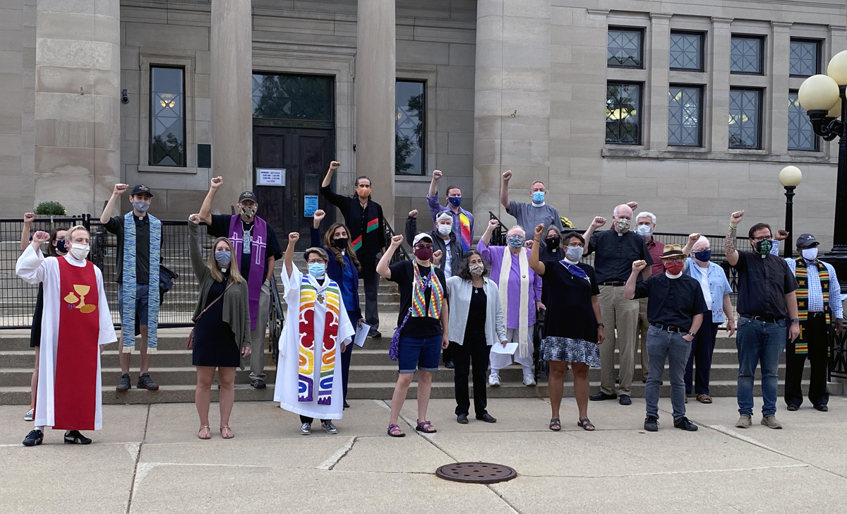 La Rvda. Grace Cajiuat (tercera de la izquierda en la primera fila), pastora de la Iglesia Metodista Unida Wesley en Kenosha, estado de Wisconsin, protesta con otros/as líderes de diferentes religiones en la Biblioteca del Parque Simmons Park a comienzos de septiembre, cuando el presidente visitó esta ciudad, cercana a Milwaukee. Foto cortesía de Chris Herigstad. La Rvda. Grace Cajiuat (tercera de la izquierda en la primera fila), pastora de la Iglesia Metodista Unida Wesley en Kenosha, estado de Wisconsin, protesta con otros/as líderes de diferentes religiones en la Biblioteca del Parque Simmons Park a comienzos de septiembre, cuando el presidente visitó esta ciudad, cercana a Milwaukee. Foto cortesía de Chris Herigstad.