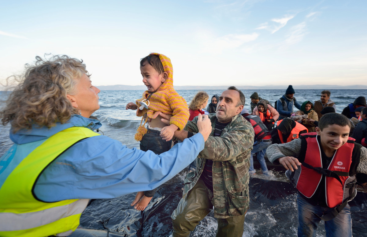 Voluntarios/as llevan a un niño a tierra en una playa cerca de Molyvos, en la isla griega de Lesbos, el 30 de octubre de 2015, después de que un grupo de refugiados/as cruzara el mar Egeo desde Turquía en un pequeño bote abarrotado de gente, proporcionado por traficantes turcos a quienes les habían pagado enormes sumas de dinero. Los/as refugiados/as fueron recibidos/as en Grecia por voluntarios/as locales e internacionales y luego se dirigieron hacia Europa occidental. Foto de archivo de Paul Jeffrey / Life on Earth Pictures.