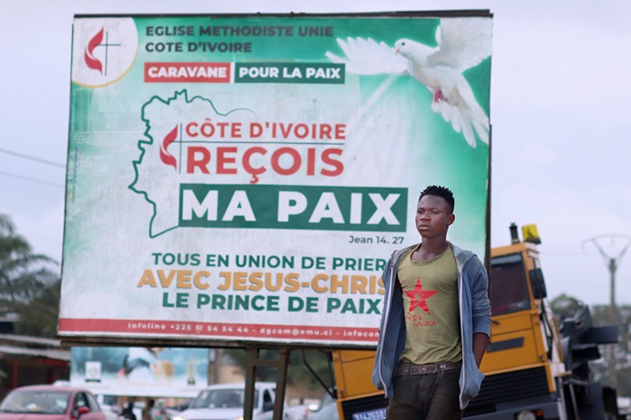 A pedestrian passes one of The United Methodist Church’s billboards calling for peace in the community of Abobo, Côte d’Ivoire. The United Methodist Church and its partners organized a communication campaign asking that the population and the authorities show restraint during the electoral period. The caravan crisscrossed several towns and hamlets in Côte d’Ivoire. Photo by Isaac Broune, UM News.