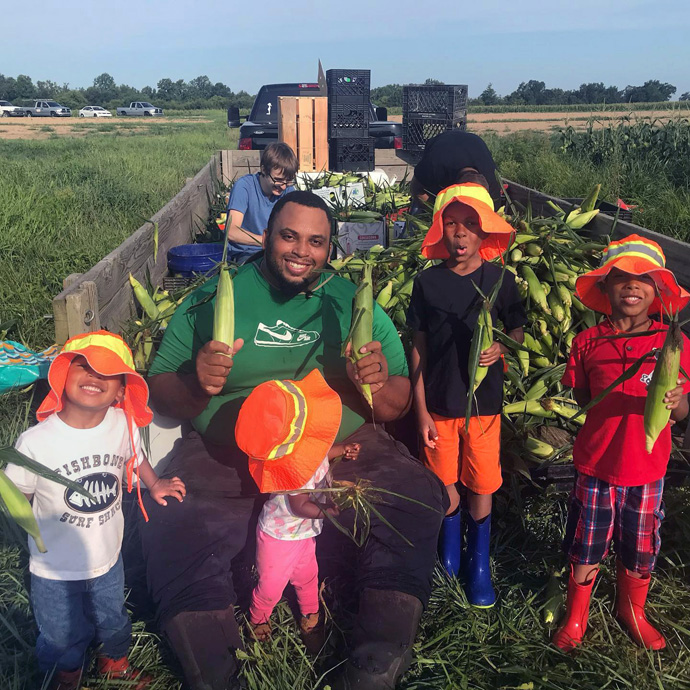 Former NFL center Jason Brown sits on the back of a flatbed truck full of corn with his children (from left) Judah, Jason, Olivia, Noah and Tre. First Fruits Farm, Browns’ farm in Louisburg, N.C., donates almost all of its harvest to the Society of St. Andrew. Photo courtesy of the Browns.