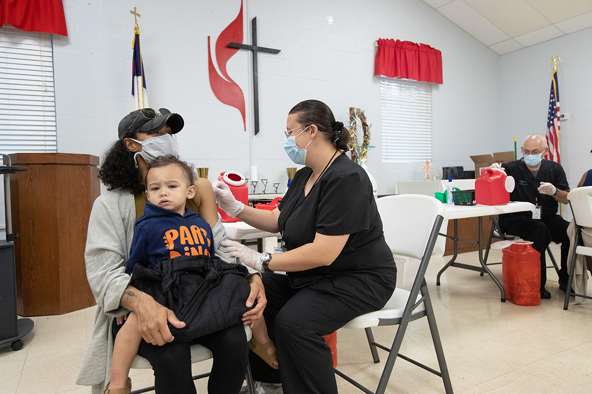 Camisha Henson sostiene a su hijo Welles en su regazo mientras recibe la vacuna COVID-19 de Tabitha England, RN, durante una clínica en la Iglesia Metodista Unida (IMU) San Marcos en Charlotte, Carolina del Norte.