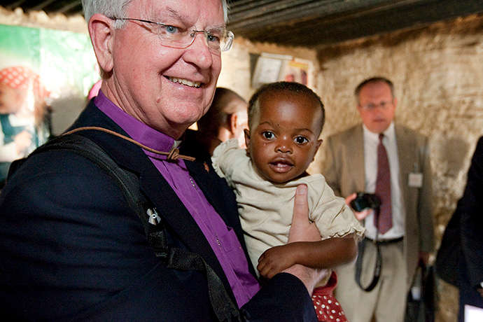 James E. Dorff, former bishop, holds 18-month-old Dunongo after her family received a mosquito net bought with funds from The United Methodist Church at their home in Lubumbashi, Congo in 2010. File photo by Mike DuBose, UM News.